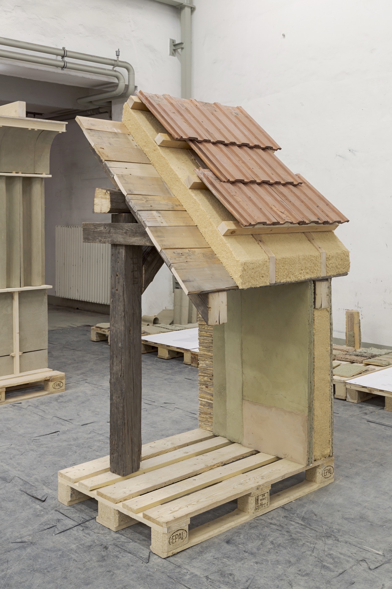 Angled view of the prototype's roof and wall assembly cut open, tile, wood-wool and timber layers exposed