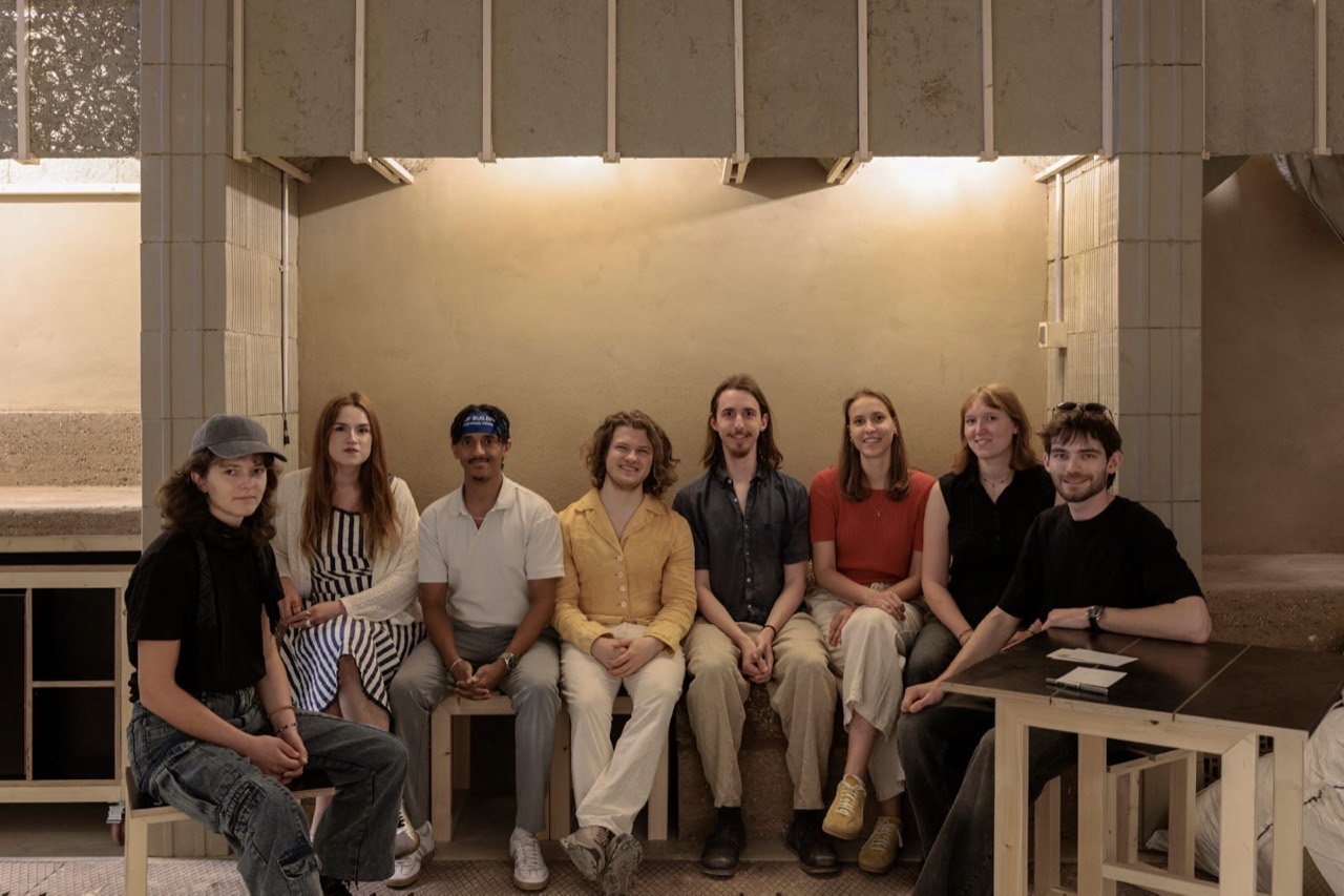 The eight-person team sitting along the finished bench under the lit knotweed panels